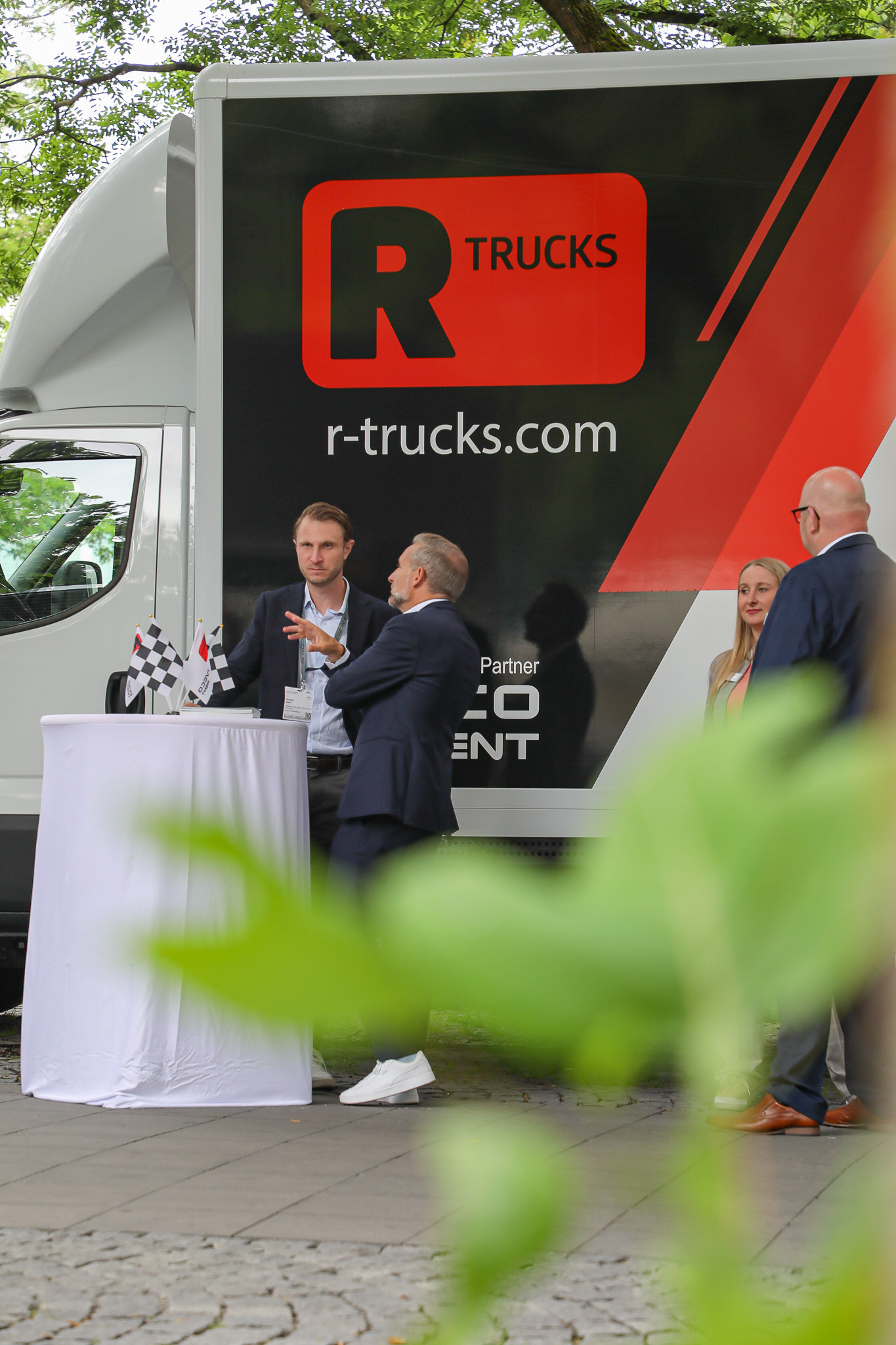 R-Trucks LKW steht draußen, davor ein weißer Tisch, an dem sich zwei Männer unterhalten