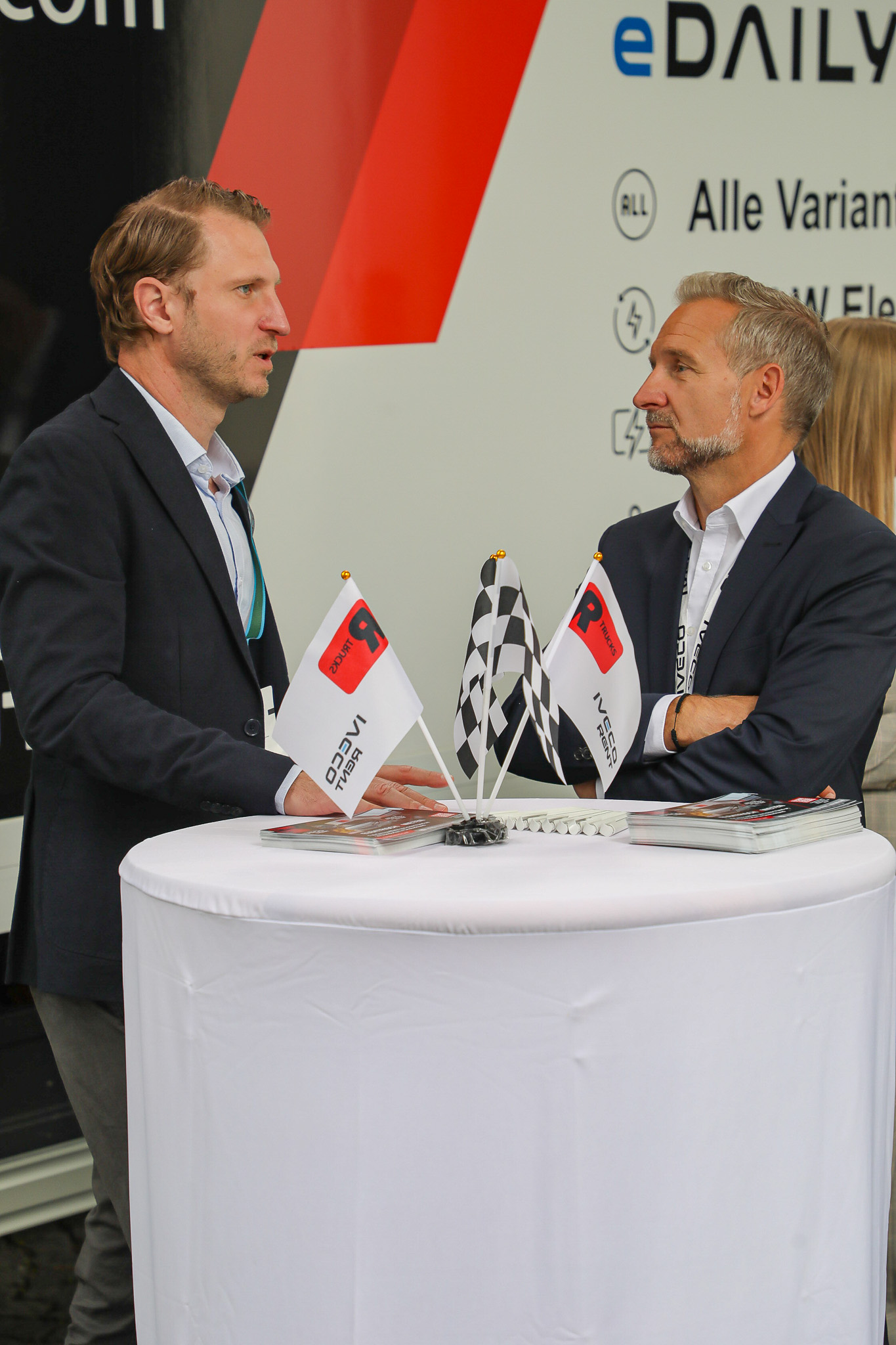 Zwei Männer unterhalten sich an einem weißen Tisch auf dem R-Trucks Messestand