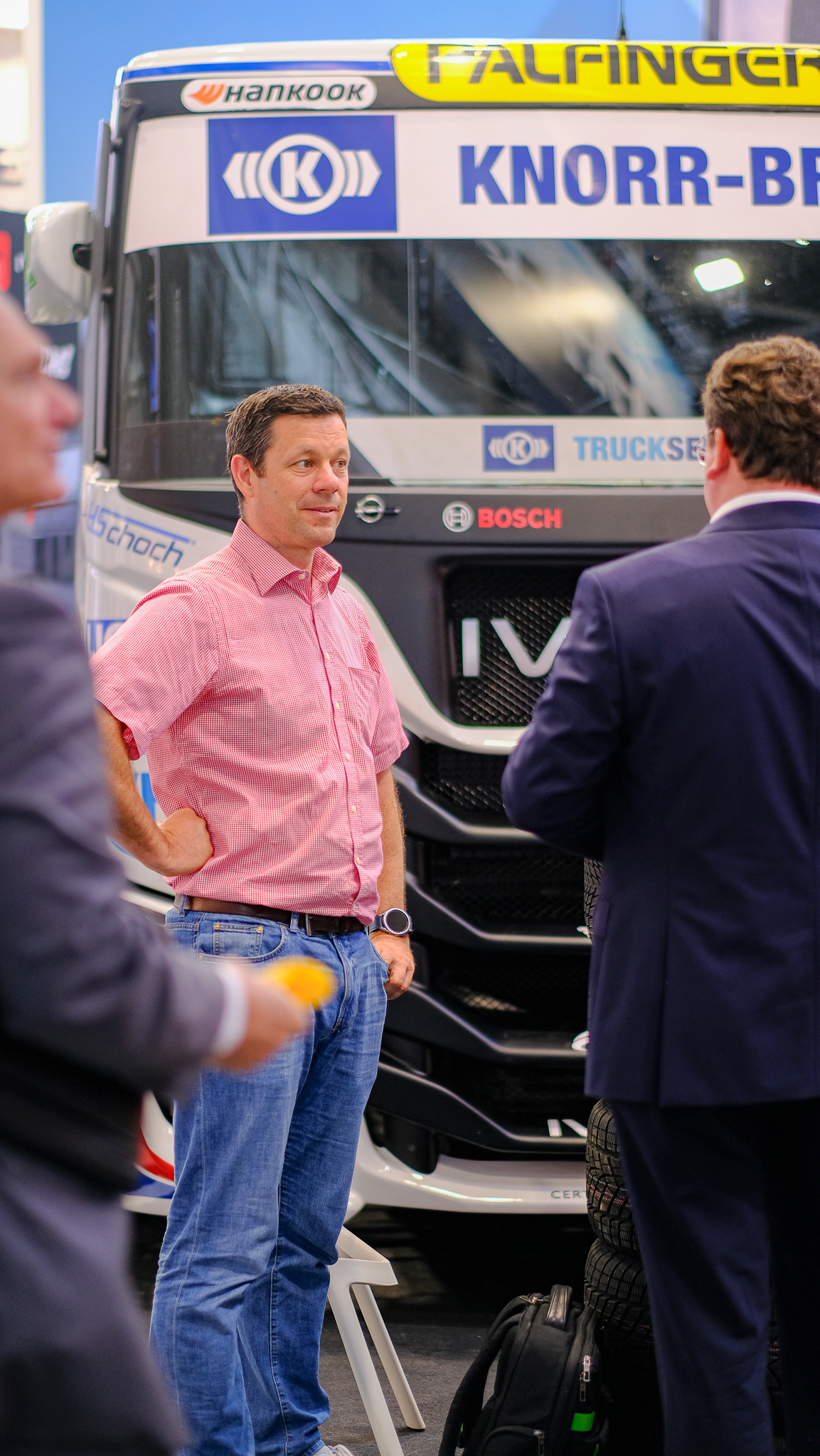 Ein Mann steht in einer Konversation zufrieden vor dem Race-Truck, der auf dem Messestand von R-Trucks steht